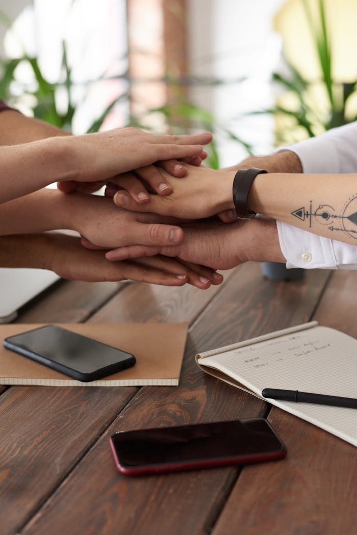 services-02 Hands from a diverse team stack on a table symbolizing unity and teamwork in a modern office setting.